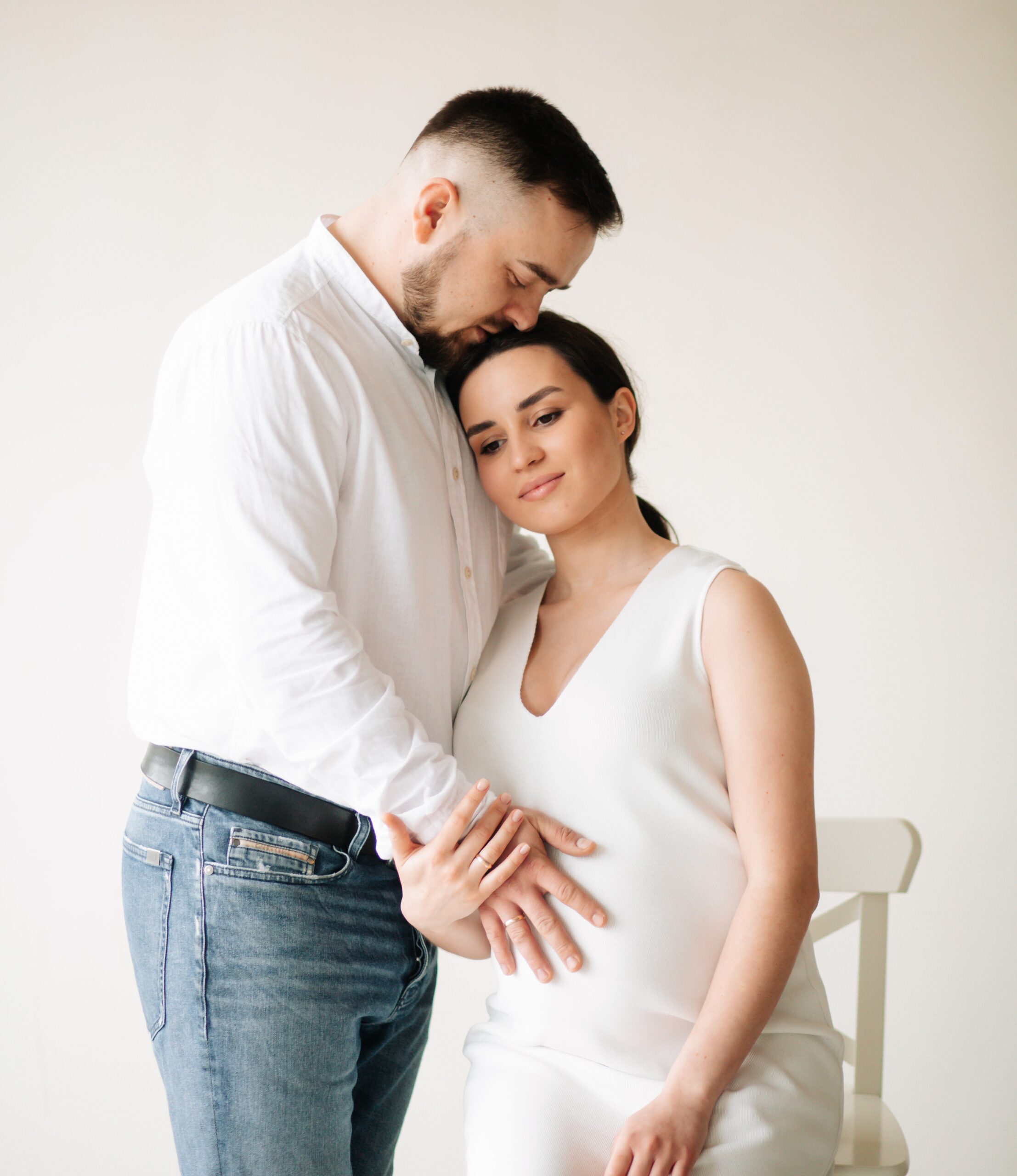 Happy pregnant woman and her husband posing together in a studio.