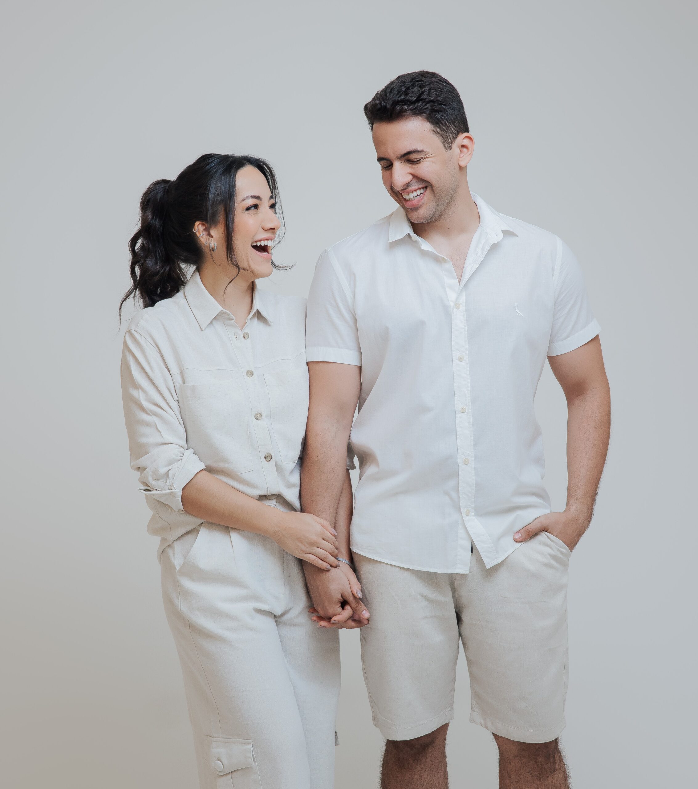 Happy couple dressed in white, with woman holding her husband's arms, hopeful about starting a family.