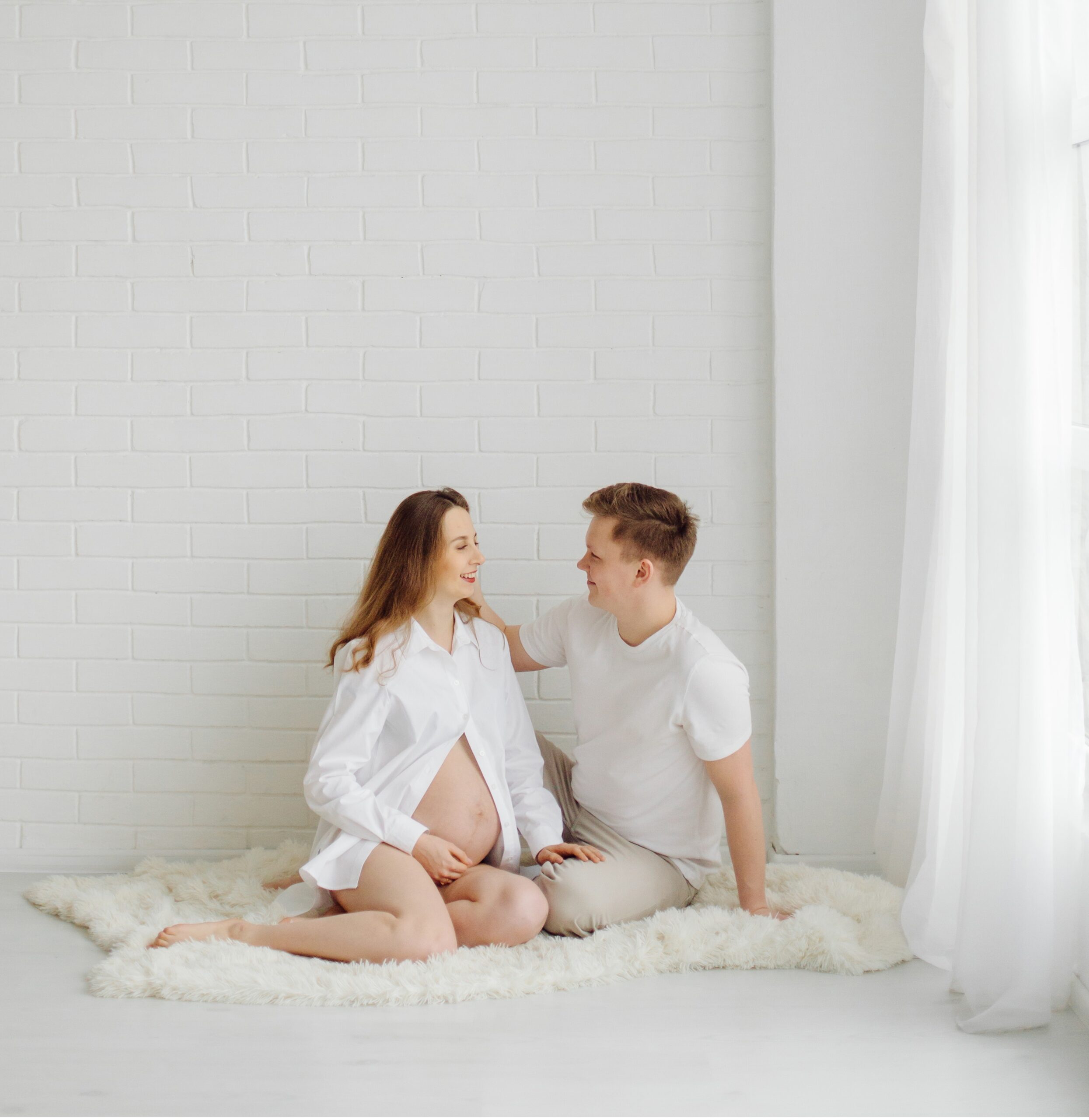 Expectant mother and her partner seated on the floor in a cozy studio maternity session.