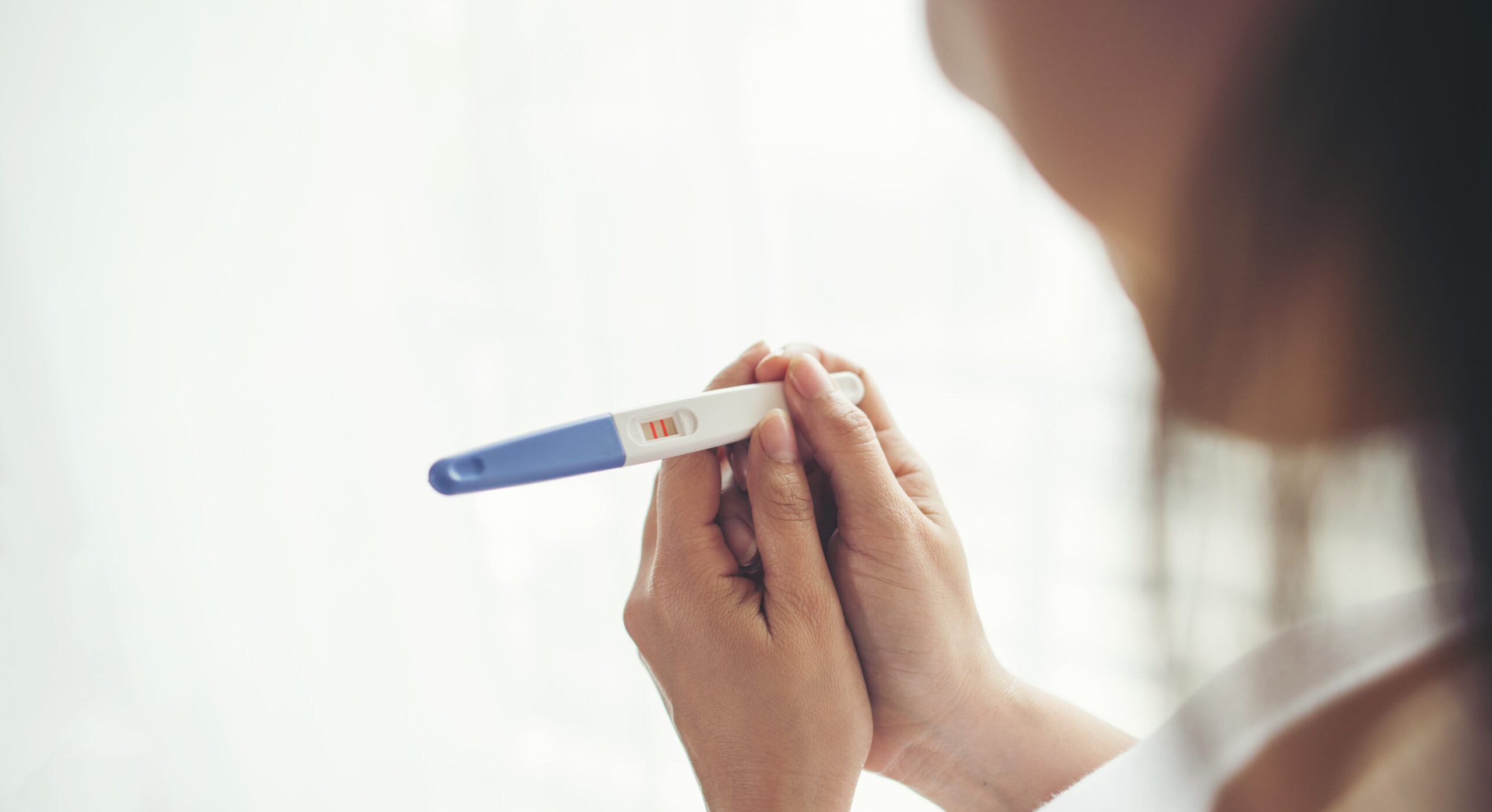 Happy woman holding a positive pregnancy test, smiling with joy.