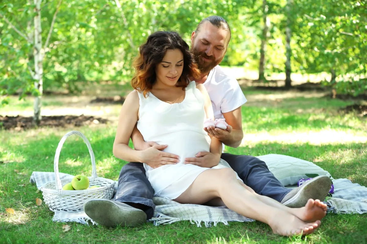 handsome-man-his-lovely-pregnant-wife-with-baby-booties-park